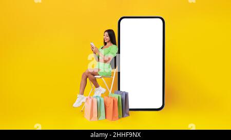 Happy lady with shopping bags sitting near mobile phone screen Stock Photo