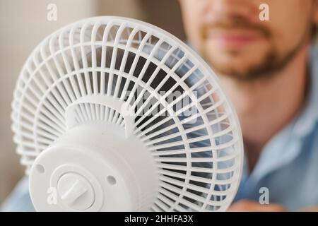 Man enjoying air flow from fan in office. Businessman refreshing in front of air electric ventilator. Summer heat. Stock Photo