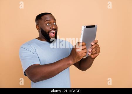 Portrait of attractive cheerful amazed guy using device gadget reading message isolated over beige pastel color background Stock Photo