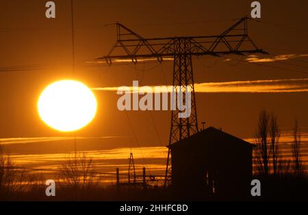 21 January 2022, Brandenburg, Großbeeren: A pole of a power line stands behind a house in the evening against the backdrop of the setting sun. Photo: Soeren Stache/dpa-Zentralbild/ZB Stock Photo