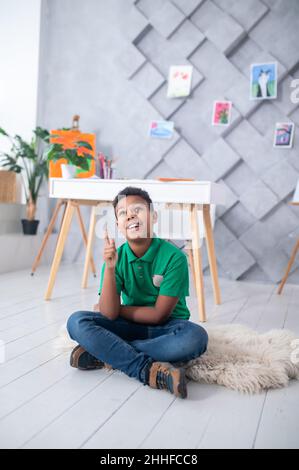 Boy sitting on floor looking pointing finger up Stock Photo