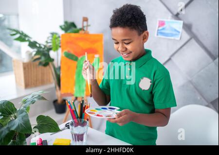 Boy looking holding paintbrush over palette with paints Stock Photo