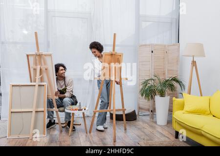 Positive african american couple looking at each other while painting on canvases at home Stock Photo