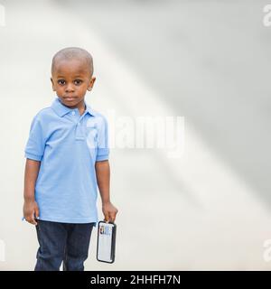 A little boy standing outside holding a cell phone and looking sad Stock Photo