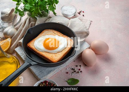 Fried egg on toast in a frying pan on a light background with spices and fresh herbs. Stock Photo