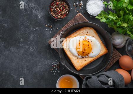 Fried eggs on toast with spices and fresh herbs on a black background. Stock Photo