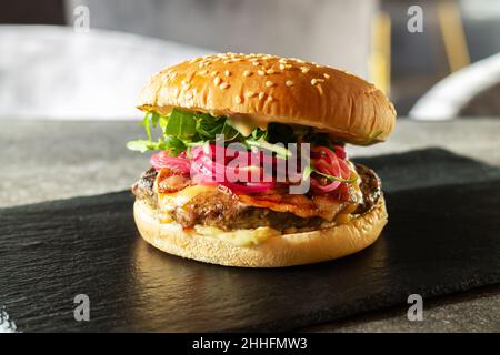 Juicy burger with beef meat, red onion, bacon, cheddar cheese, sauce, lettuce and fresh sesame bun on fast food restaurant table Stock Photo