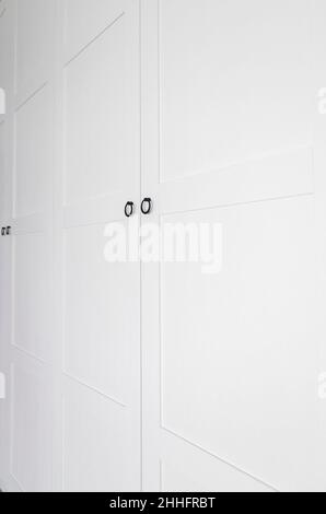 White vintage wardrobe with crown moldings wooden shelves and drawers and open facade door in light empty room Stock Photo