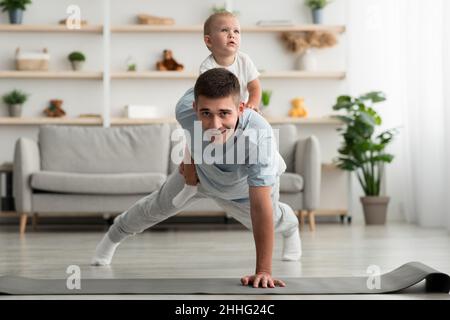 Domestic Workout. Happy Man Doing Push Up Exercise With Baby On Back Stock Photo
