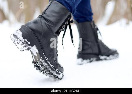 Female legs in black leather lace-up boots on a snow. Woman walking on winter street, warm footwear for cold weather Stock Photo