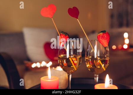 Valentines day celebration at home with champagne wine glasses with strawberries on top and red hearts surrounded with candles Stock Photo