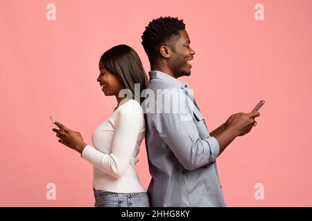 positive black couple standing back to back, using smartphones Stock Photo