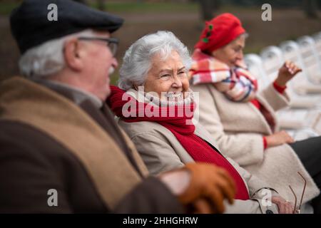 Group of happy senior friends sitting on bench in town park in autumn. Stock Photo