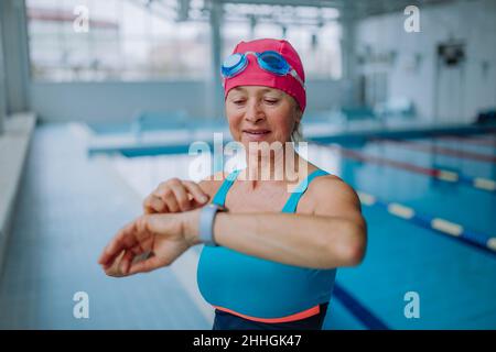 Senior woman setting smartwatch before swim in indoors swimming pool. Stock Photo