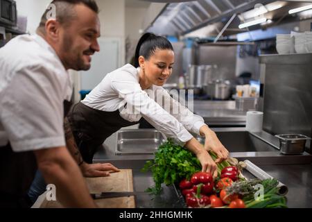 Chefs preparing vegetables for cutting in commercial kitchen. Stock Photo