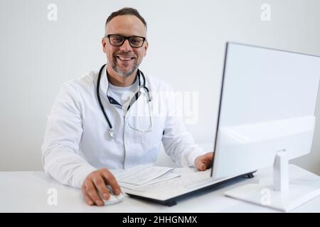Portrait of a middle-aged male doctor in eyeglasses working in the office at the computer Stock Photo