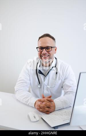 Portrait of a happy male doctor sitting at his desk in the office Stock Photo