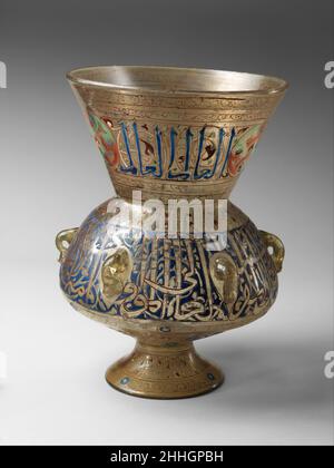 Mosque Lamp 14th century One of the conventions of Mamluk mosque lamp decoration was to execute one inscription band in blue and the other in reserve against a blue ground. On this lamp, the neck and foot repeat the phrase al?'alim ('The Wise'), punctuated by an as yet unassigned emblem, while the body bears a formulaic dedicatory inscription but no name.. Mosque Lamp. 14th century. Glass, colorless with yellow tinge; blown, applied blown foot, enameled and gilded. Attributed to Egypt or Syria. Glass Stock Photo