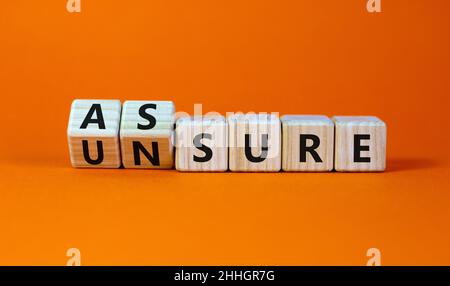 Assure or unsure symbol. Turned wooden cubes and changed the concept word unsure to assure. Beautiful orange table, orange background, copy space. Bus Stock Photo