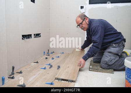 Senior mason laying ceramic wood effect tiles. Stock Photo