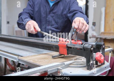 Tiler hands cutting a ceramic wood effect tile with a manual tile cutter. Stock Photo