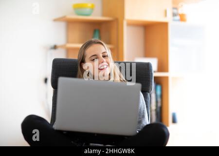 Smiling young woman using laptop at home Stock Photo