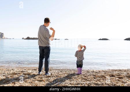 Rear view of father and son skipping stones on lakeshore Stock Photo