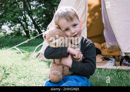 Portrait of boy hugging teddy bear in front of tent Stock Photo