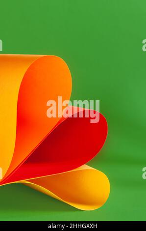 Yellow, orange and red colorful paper swirl on green background Stock Photo