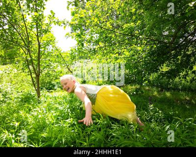 Adorable happy laughing little girl in yellow dress playing in a summer park. Stock Photo