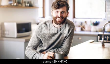 Coffee gets my day going. Shot of a handsome young man having a cup of coffee in the kitchen at home. Stock Photo