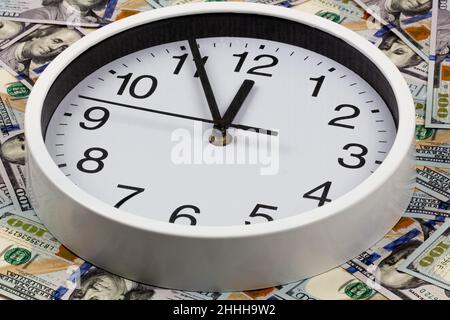 Time is money. A large white watch with black numbers is surrounded by hundred dollar bills. Business and finance concept. The clock shows the time Stock Photo