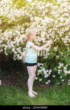 Beautiful teenager blonde girl make selfie on blooming spring magnolia trees background with white fragrant flowers Stock Photo
