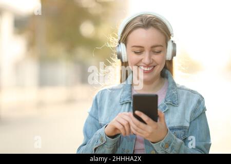 Front view of happy teen wearing headphones listening to music walking outdoors Stock Photo