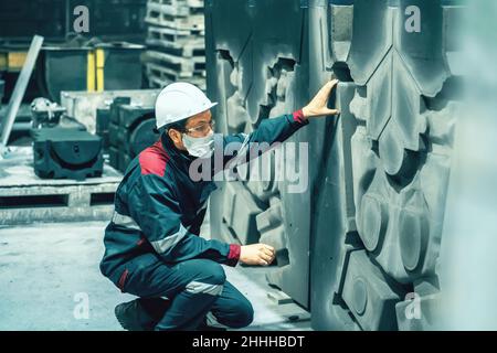 Quality control inspector in factory. Unrecognizable engineer in hard hat, workwear and face mask in workplace in metallurgy plant. Stock Photo