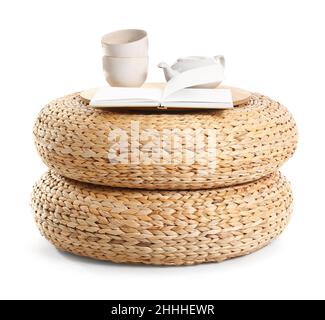 Opened book, cups and teapot on wicker poufs against white background Stock Photo