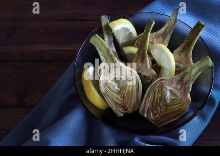 Fresh organic artichokes cut in halves with lemons on dark wooden background. Directly above. Stock Photo