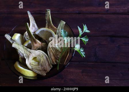 Fresh organic artichokes cut in halves with lemons on dark wooden background. Directly above. Stock Photo