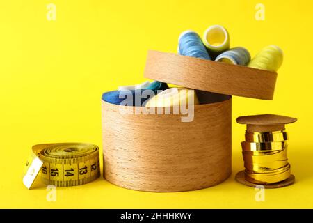 Wooden box with sewing thread spools, measuring tape and golden ribbon on color background Stock Photo