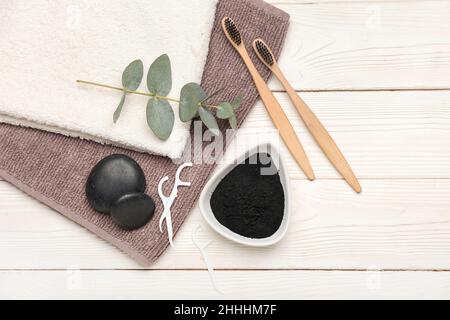 Bowl with activated charcoal tooth powder, towels and brushes on white wooden background Stock Photo