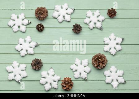 Frame made of snowflakes and pine cones on green wooden background Stock Photo