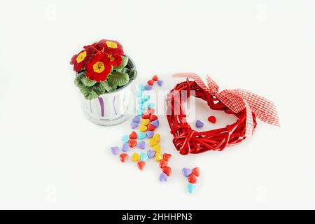 braided heart on a light background with a red primrose flower. a heart woven from dried branches of handmade grapes is a background for congratulatio Stock Photo