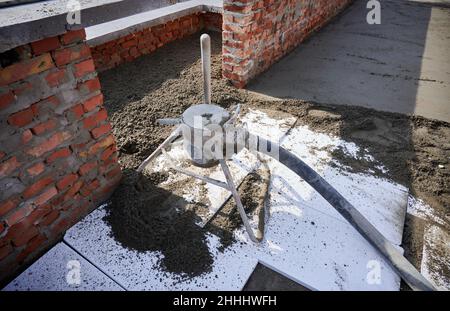 Building with concrete floor covered with sand-cement mix and professional equipment. Preparation of floor screed mixture with mortar mixer machine in new building at construction site. Stock Photo