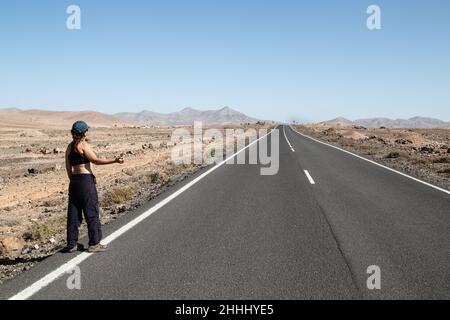 Woman hitchhiking alone on desert road. Stock Photo