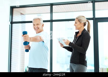 Keeping track of his progress. Shot of a physiotherapists helping her senior patient with his exercises in a fitness center. Stock Photo