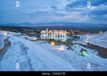 Pamukkale travertines in foreground. Sunset sky and illuminated houses in background. Stock Photo