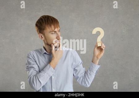 Young handsome caucasian male isolated on gray background holding question mark symbol Stock Photo