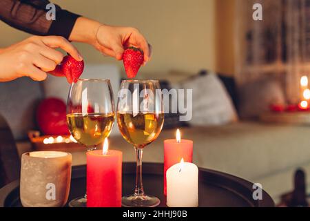 Woman decorating table setting for Valentines day celebration at home putting strawberries on glasses with wine by candles on table. Night date. Space Stock Photo