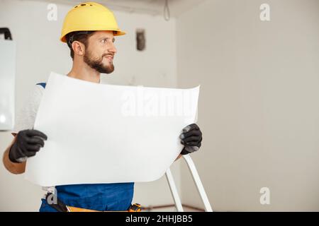 Portrait of thoughtful construction worker in hardhat looking away while studying blueprint, standing in new apartment Stock Photo