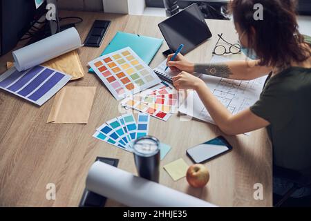 Working process of female interior designer making notes in her notebook, choosing color samples, sitting at the table in her office Stock Photo